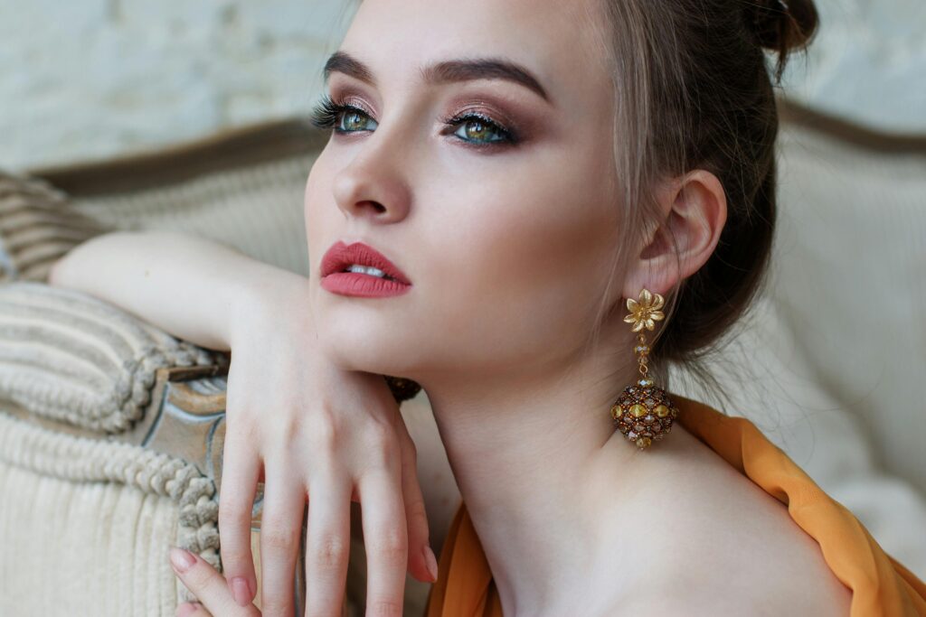 Mulher elegante com maquiagem sofisticada e brinco dourado, olhando para o alto em ambiente refinado.